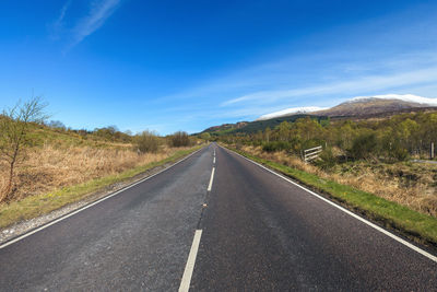 Empty road along trees and against blue sky