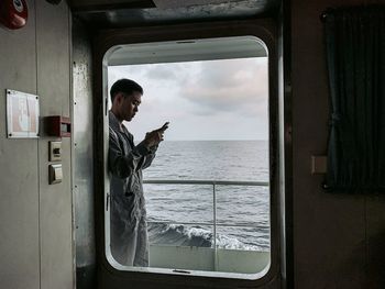 Side view of man in sea against sky seen through window