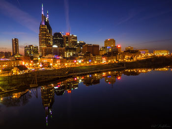 Illuminated buildings by river against sky at night