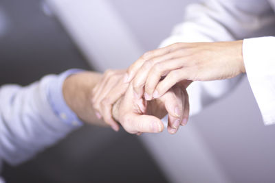 Cropped image of doctor examining hand against wall