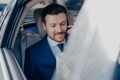 Close-up of smiling businessman talking on phone sitting at car