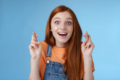Happy woman with fingers crossed against blue background