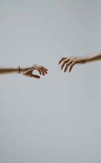 Cropped hand of man reaching for girlfriend against gray background