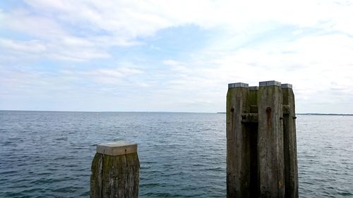 Wooden posts in sea against sky