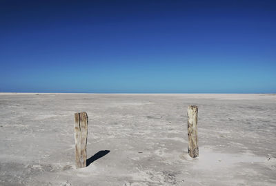 Wooden post on snow covered land against clear blue sky