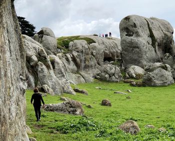 Rear view of woman walking by cliff against sky