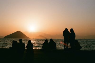 Silhouette people on shore at beach against sky during sunset