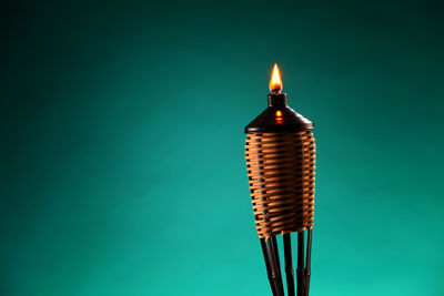 Close-up of illuminated tiki torch against green background