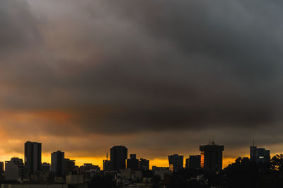 Silhouette buildings against dramatic sky during sunset