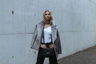 Portrait of young woman standing against wall