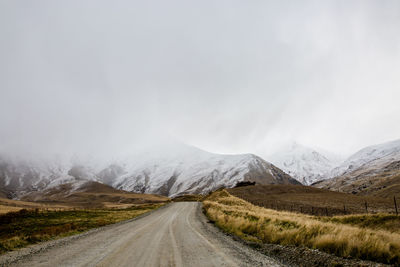 Country road leading towards snowcapped mountains against sky