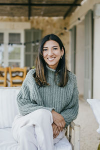 Portrait of happy woman sitting on sofa in backyard patio