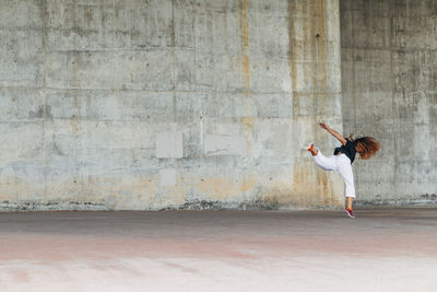 Young woman doing acrobatic jump while exercising against wall