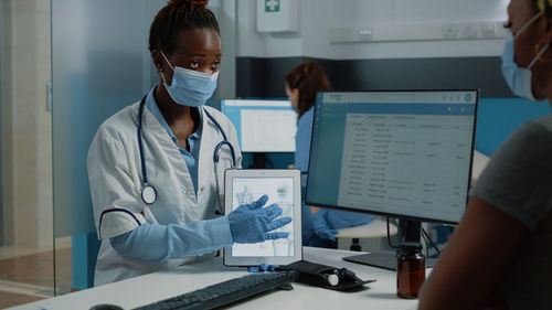 Doctor wearing mask showing digital tablet in office