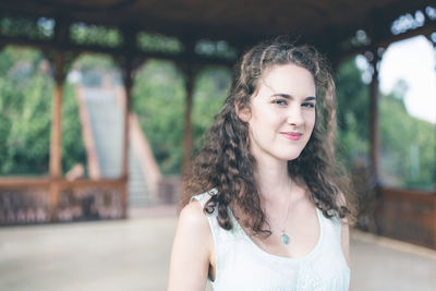 Beautiful curly hair young woman in a light blue simple dress in a pavilion in summer garden