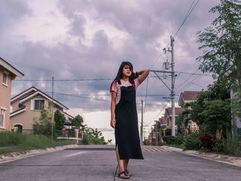 Full length of woman standing on road against cloudy sky