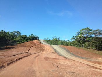 Road amidst trees against clear blue sky