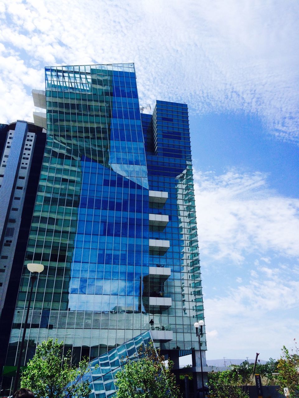 building exterior, architecture, built structure, low angle view, modern, city, sky, office building, skyscraper, building, tall - high, tower, day, cloud - sky, blue, outdoors, no people, glass - material, tree, reflection