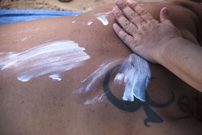 Cropped hand of person applying lotion on man back lying at beach