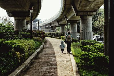 Rear view of mother and daughter walking on footpath amidst bridges