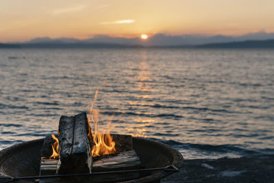 Wood burning against sea during sunset