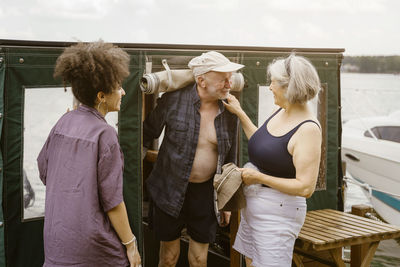 Smiling senior couple near young woman standing on houseboat