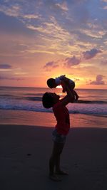 Side view of woman with boy at beach against sky during sunset