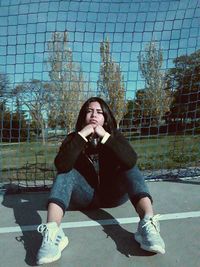 Full length of teenage girl sitting by fence