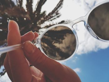 Cropped hand of woman holding sunglasses against sky