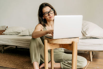 Young woman using laptop while sitting on sofa at home