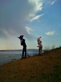 Men standing on rock by sea against sky