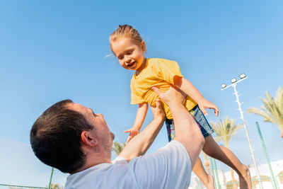 Happy father throwing up baby against blue sky