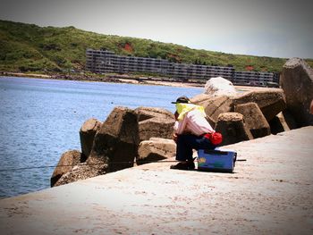 Rear view of woman standing on rock by sea against clear sky