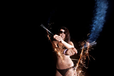 Woman in bikini playing with firework at night