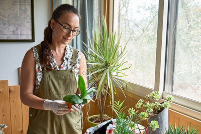 Midsection of woman standing by potted plant against window