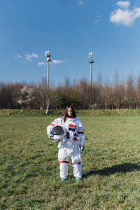 Female astronaut holding space helmet on grass area