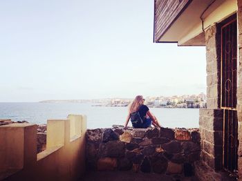 Rear view of woman sitting by sea against sky