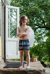 Full length portrait of shirtless boy, standing against tree, pretending, he is an angel