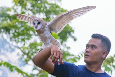 Mid adult man holding owl while standing against clear sky