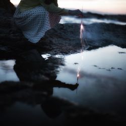 Girl holding fire cracker reflected in water