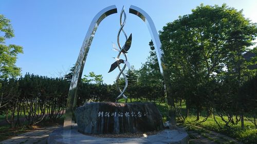 Statue hanging by trees against sky