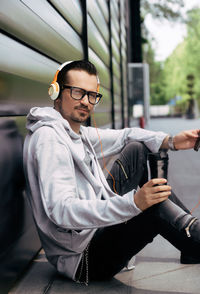 Smiling man listening music over headphones while drinking takeaway coffee in the city,