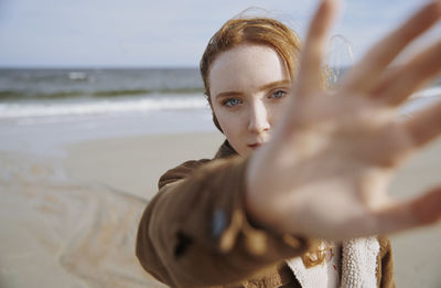 Redhead teenage girls gesturing at beach on sunny day