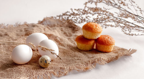 White chicken eggs, a quail egg, stems of dried grass and three cupcakes on a burlap bag