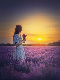 Rear view of woman standing against sky during sunset