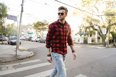 Man wearing plaid shirt and sunglasses while walking on road