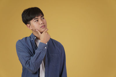 Portrait of young man looking away against orange background