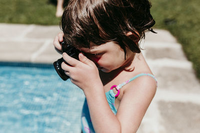 Side view of girl photographing by swimming pool