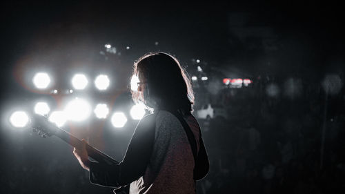 Side view of woman playing guitar at night