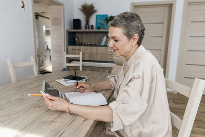 Woman using digital tablet and taking notes at table at home